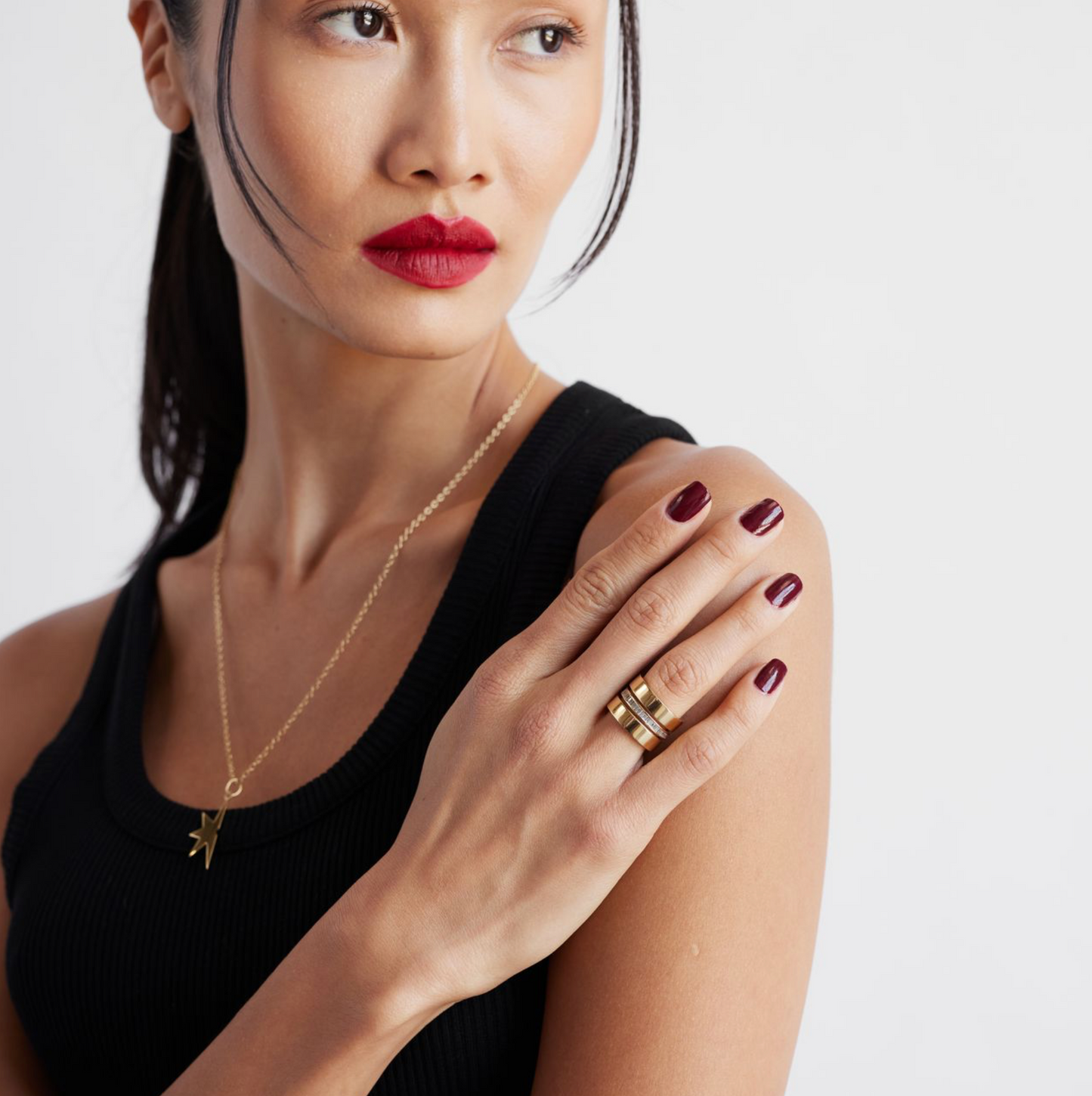 A person wearing a black top and showcasing a gold ring with a black enamel detail on the finger.