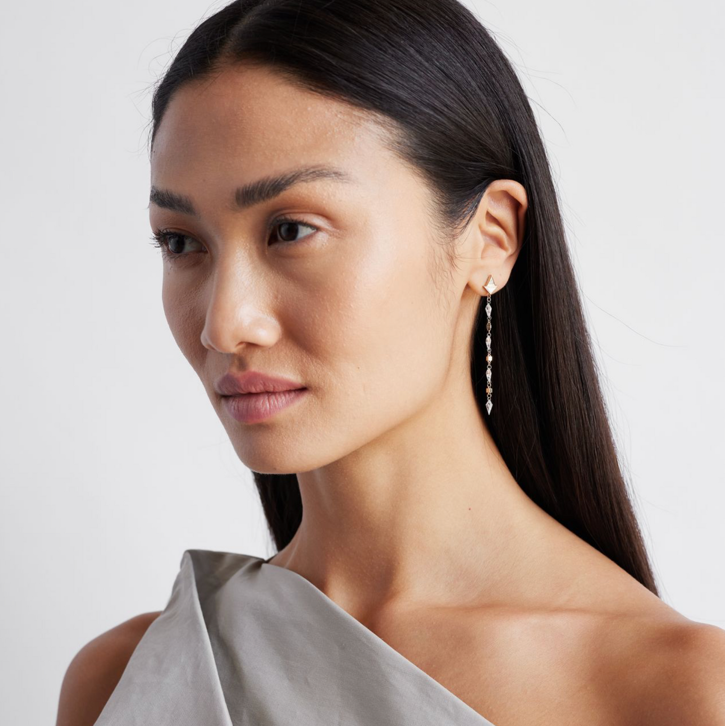 A model wearing a pair of white gold earrings featuring kite-shaped white diamonds and white enamel details.
