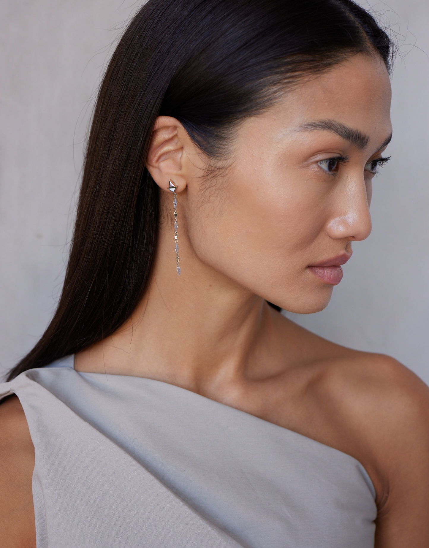 A model wearing a pair of white gold earrings featuring kite-shaped white diamonds and white enamel details.