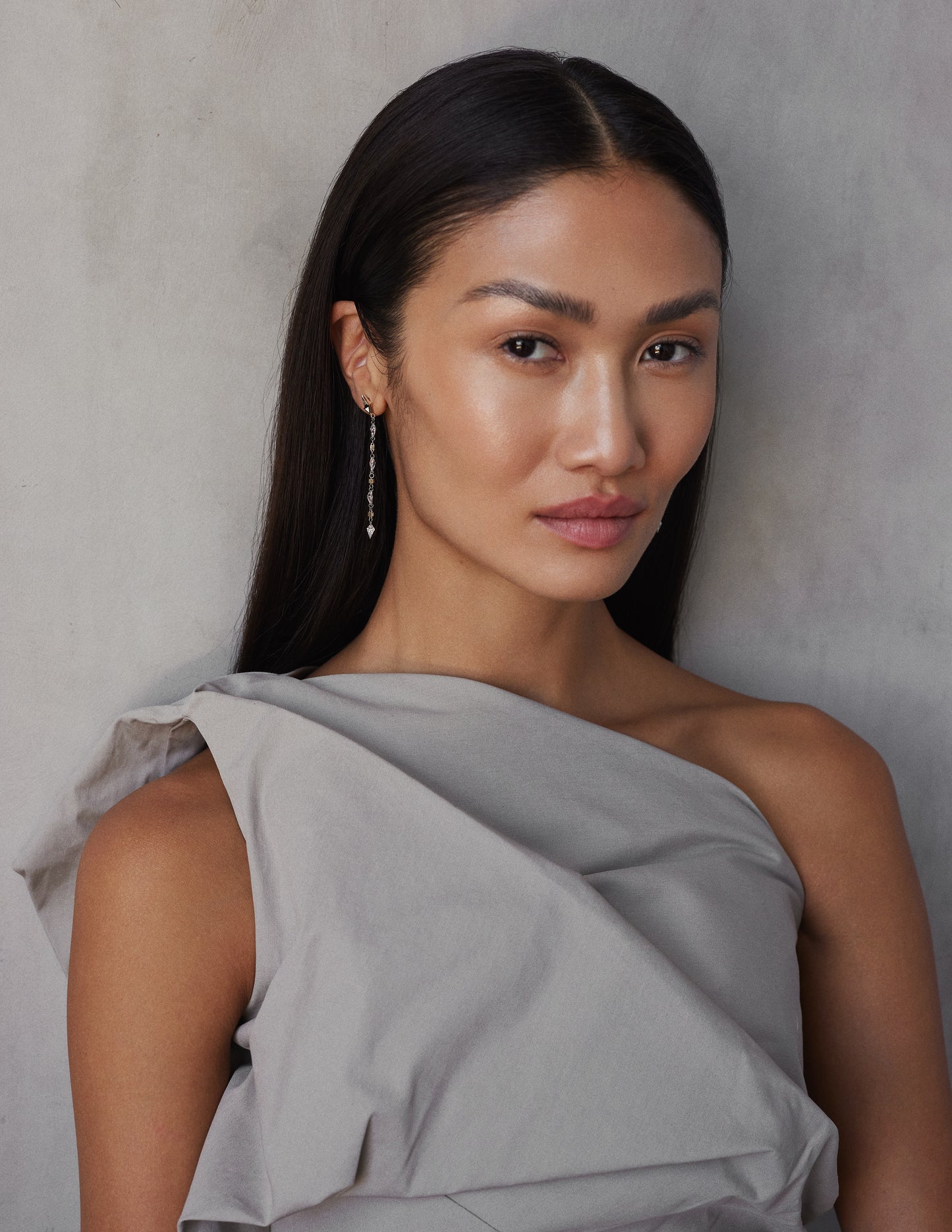 A model wearing a pair of white gold earrings featuring kite-shaped white diamonds and white enamel details.