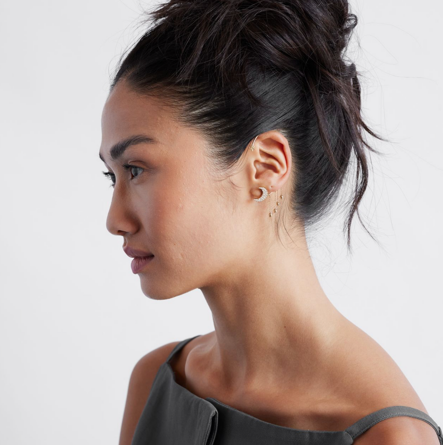 model wearing a gold ear cuff featuring a crescent moon design with pavé diamonds and dangling gold balls on a white background.