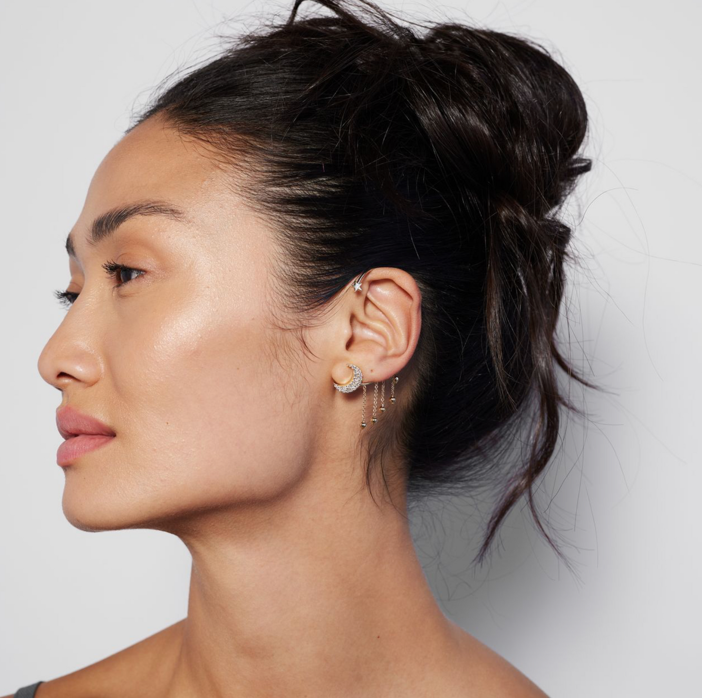 model wearing a gold ear cuff featuring a crescent moon design with pavé diamonds and dangling gold balls on a white background.