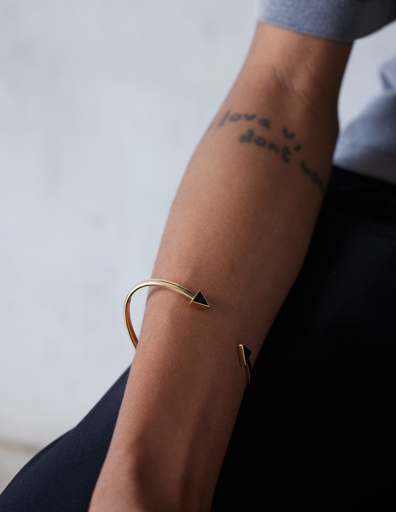 A person showing their forearm with a gold bracelet featuring black enamel piping and chunky black arrow tips.