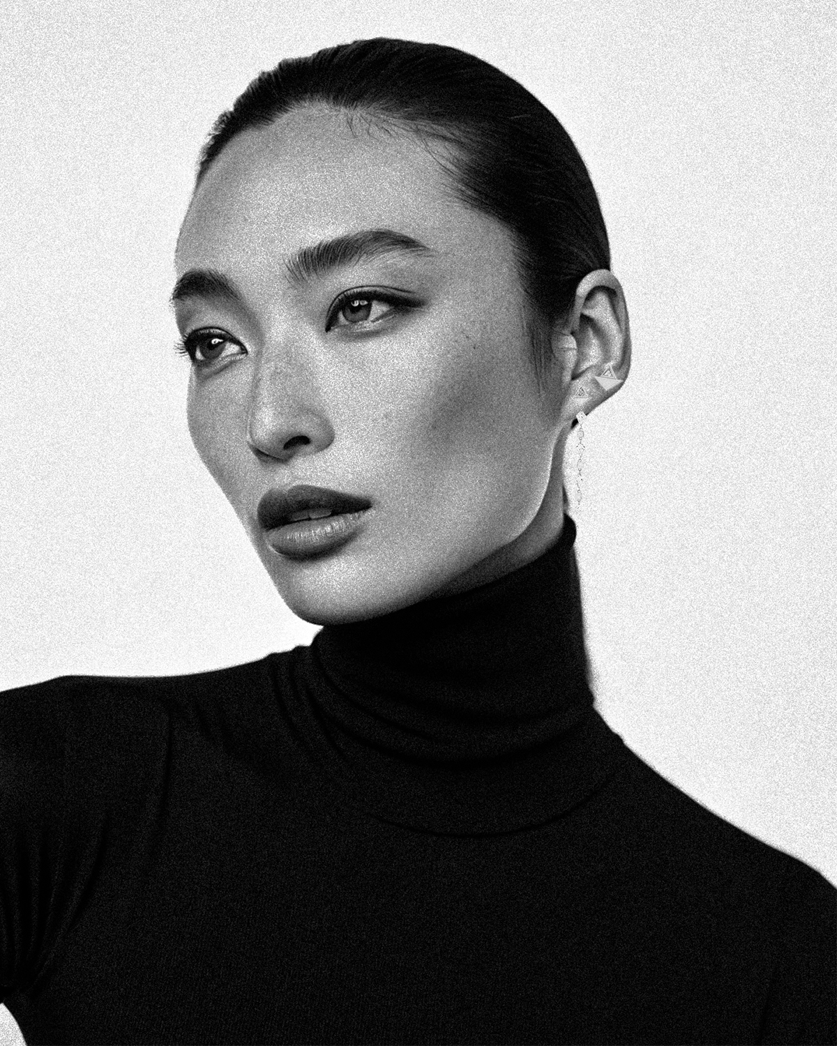 Black and white portrait of a person wearing a black turtleneck against a light background wearing asymmetric pair of earrings on one ear diamonds and white gold