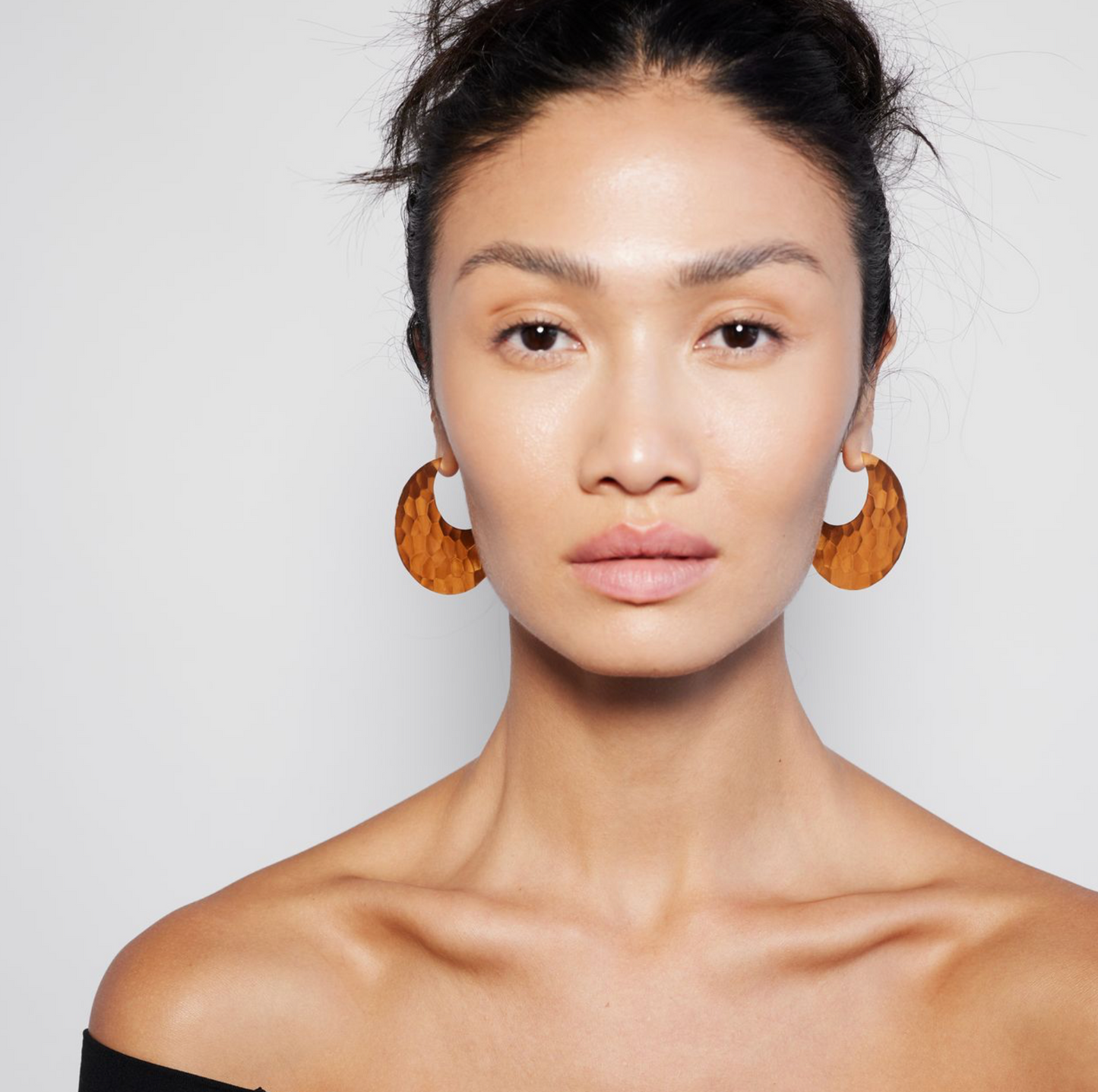 A person wearing a pair of gold hoop earrings.