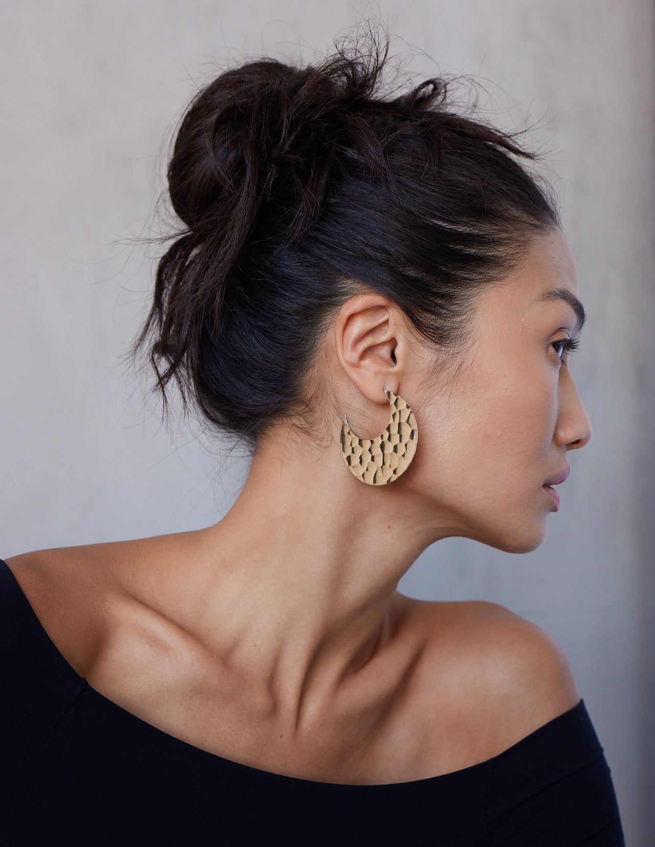 A model wearing a pair of 14K solid gold hammered hoop earrings with a textured surface, displayed against a white background.