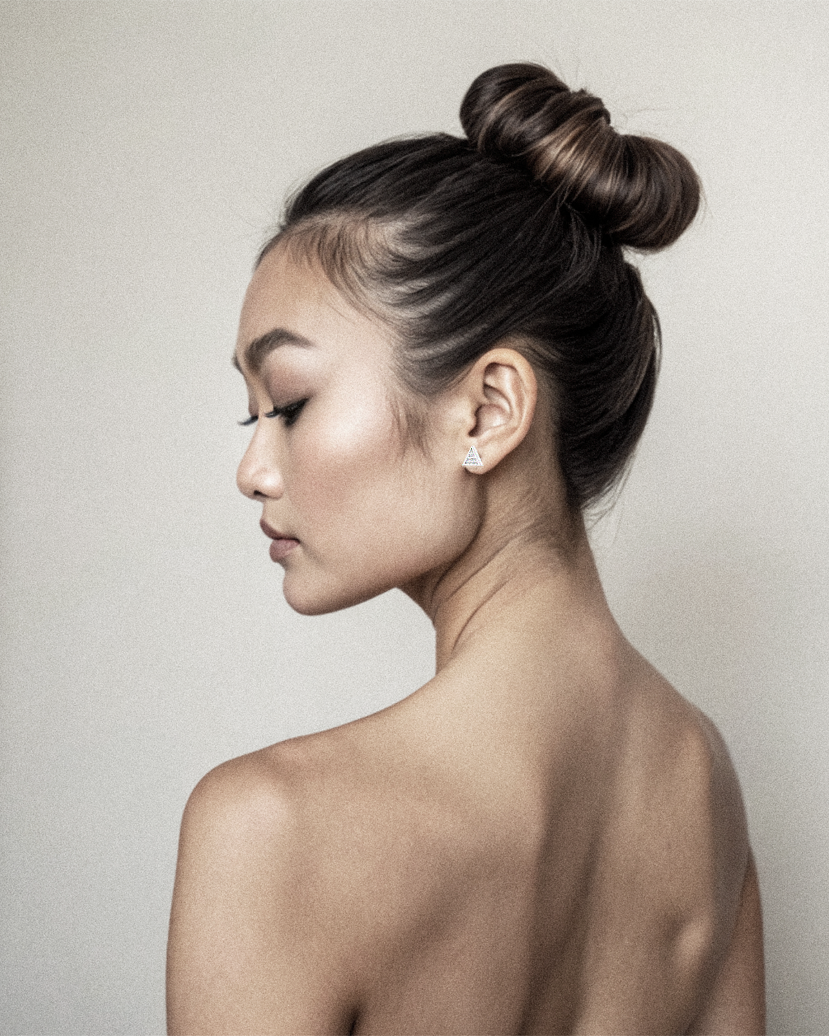 Woman with styled hair in a bun and triangle white gold studs with baguette and trillion diamonds set against a plain background