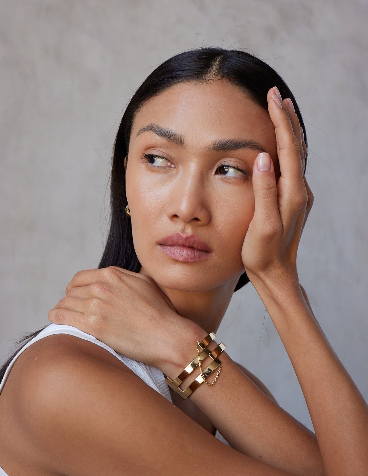 A person wearing a white top and a bold gold cuff bracelet with a chain and pin clasp.