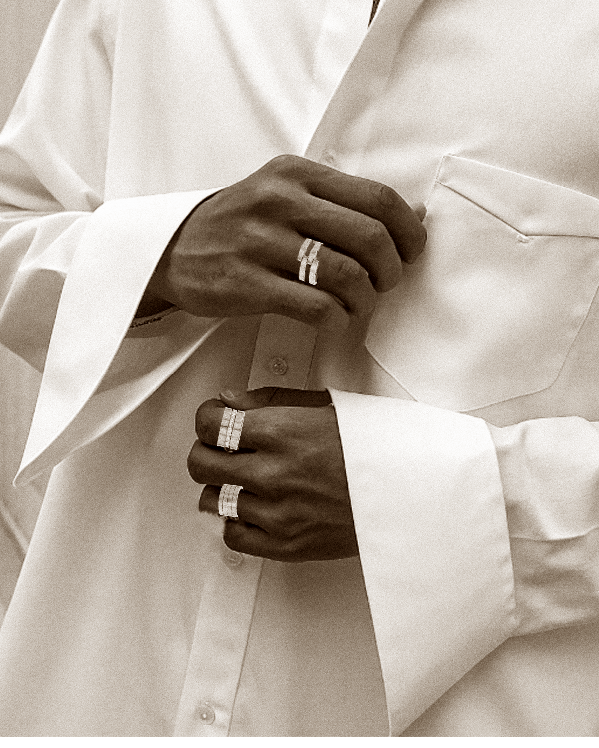 Close-up of a person wearing a white shirt with rolled-up sleeves and yellow gold rings on their fingers.