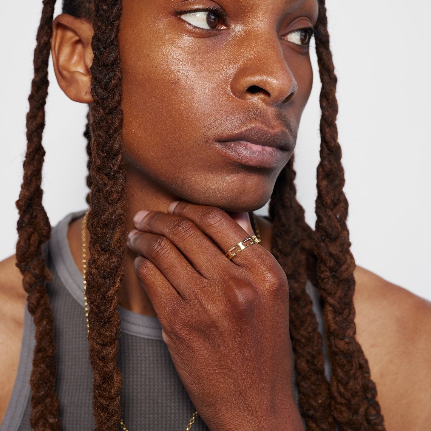 A close-up image of a person with their hand touching their chin, wearing a gold ring on their ring finger.
