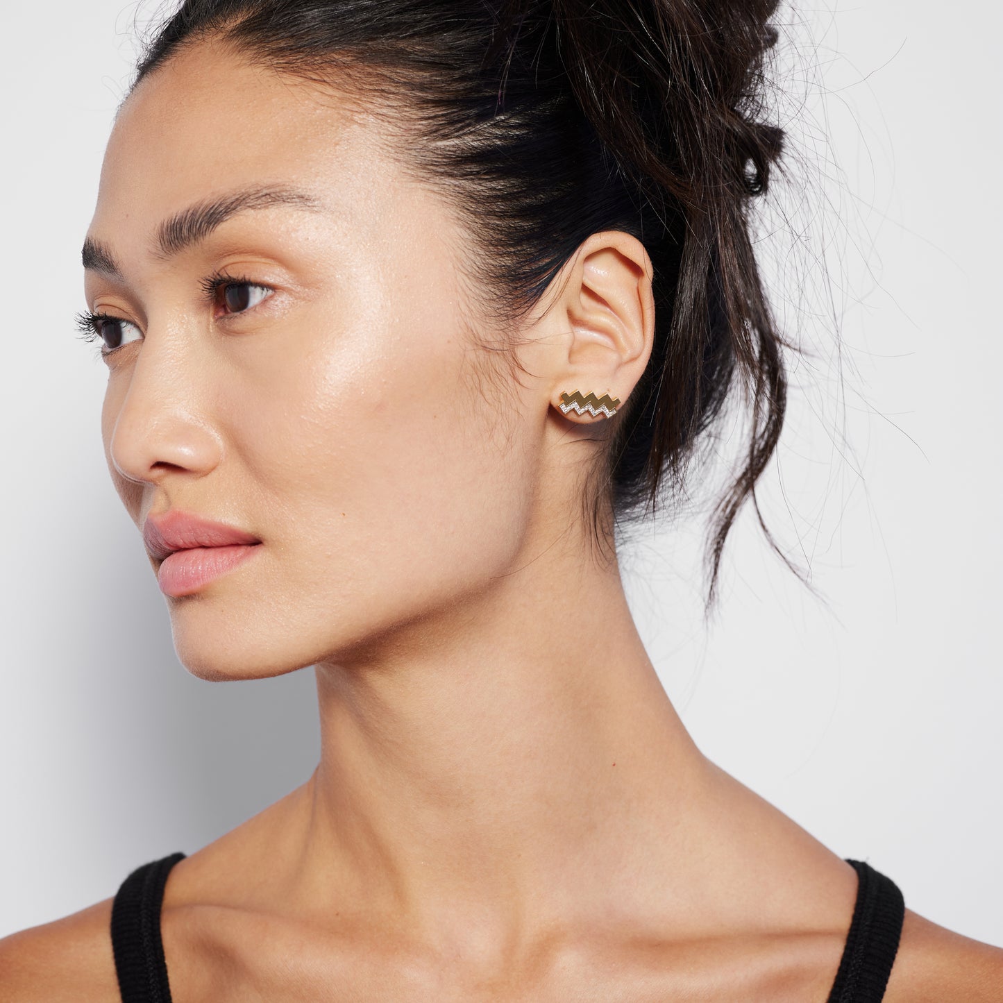 A person wearing a single gold stud earring with a diamond pattern.