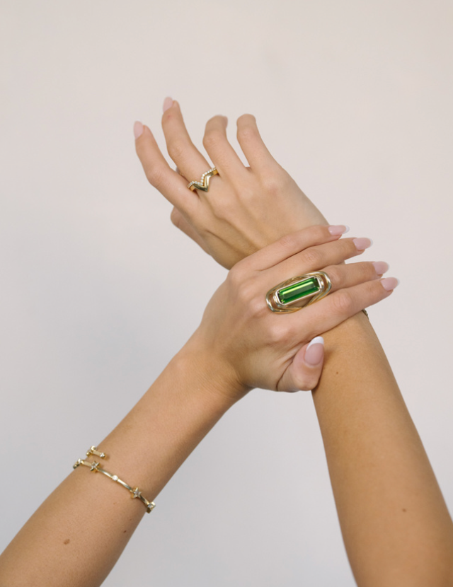 A LÖF gold ring featuring a large green tourmaline stone with a unique swooping band design.