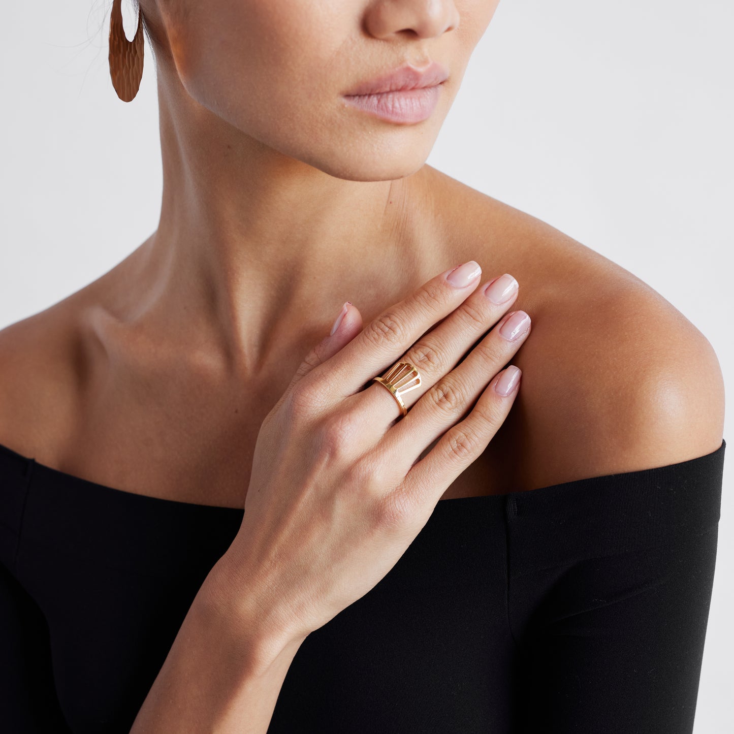 A person wearing a black off-shoulder top showcasing a gold ring on their left hand's finger.
