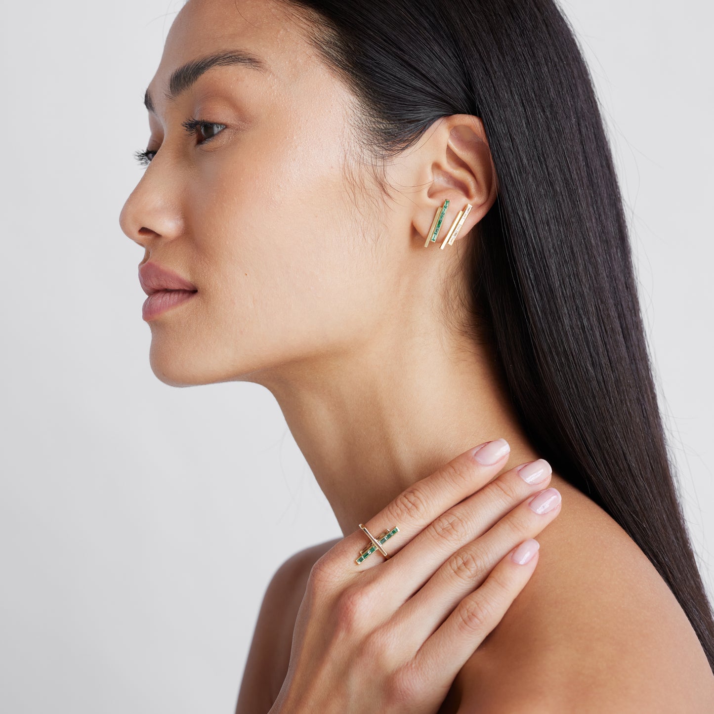 A model wearing a pair of gold stud earrings with pinstripe bar design set with either diamonds or emeralds.
