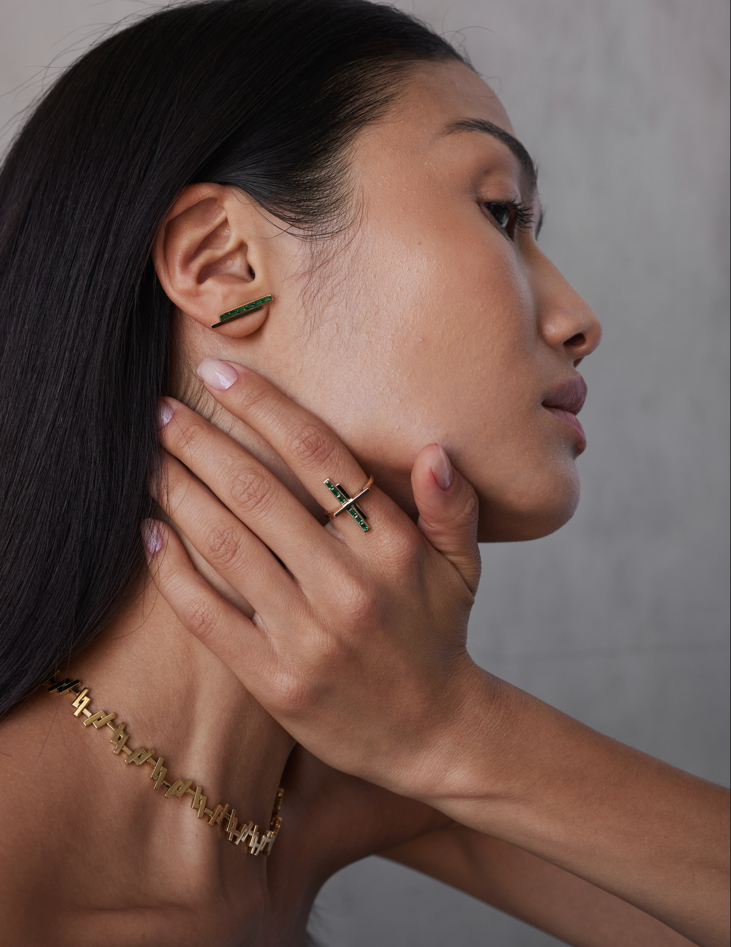 A model wearing pair of gold stud earrings with pinstripe bar design set with either diamonds or emeralds.