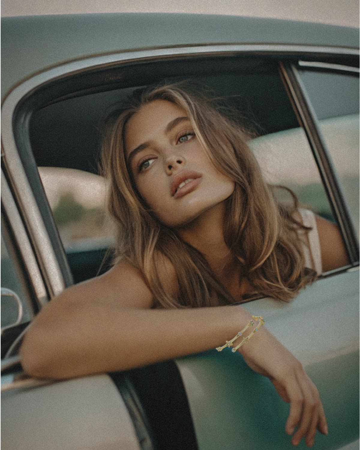 Woman leaning out of a car window with a vintage car interior wearing a wrap around bracelet