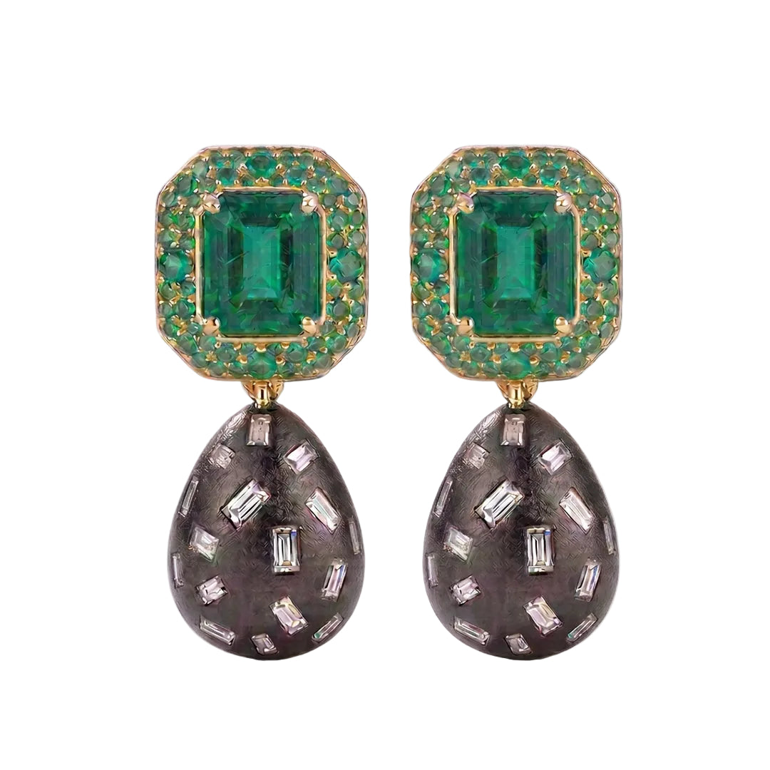 A pair of drop earrings featuring rectangular emerald-cut emeralds surrounded by small green stones in gold-toned settings, with teardrop-shaped dark gray pavé drops set with clear baguette and round stones, shown on a white background.