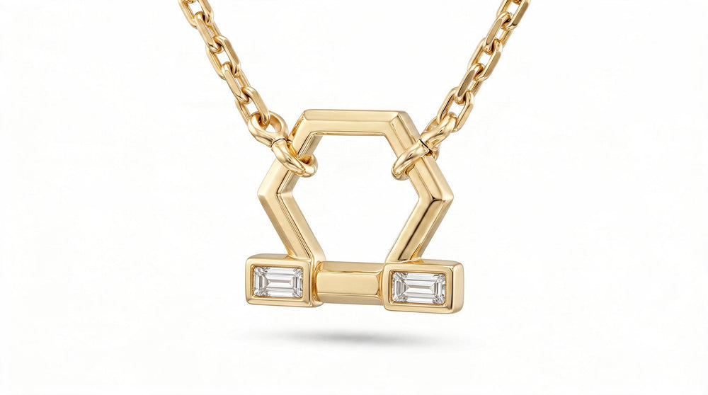 A gold geometric pendant necklace featuring a hexagonal design with two rectangular bezel-set clear baguette diamonds, suspended from a delicate gold chain against a white background.