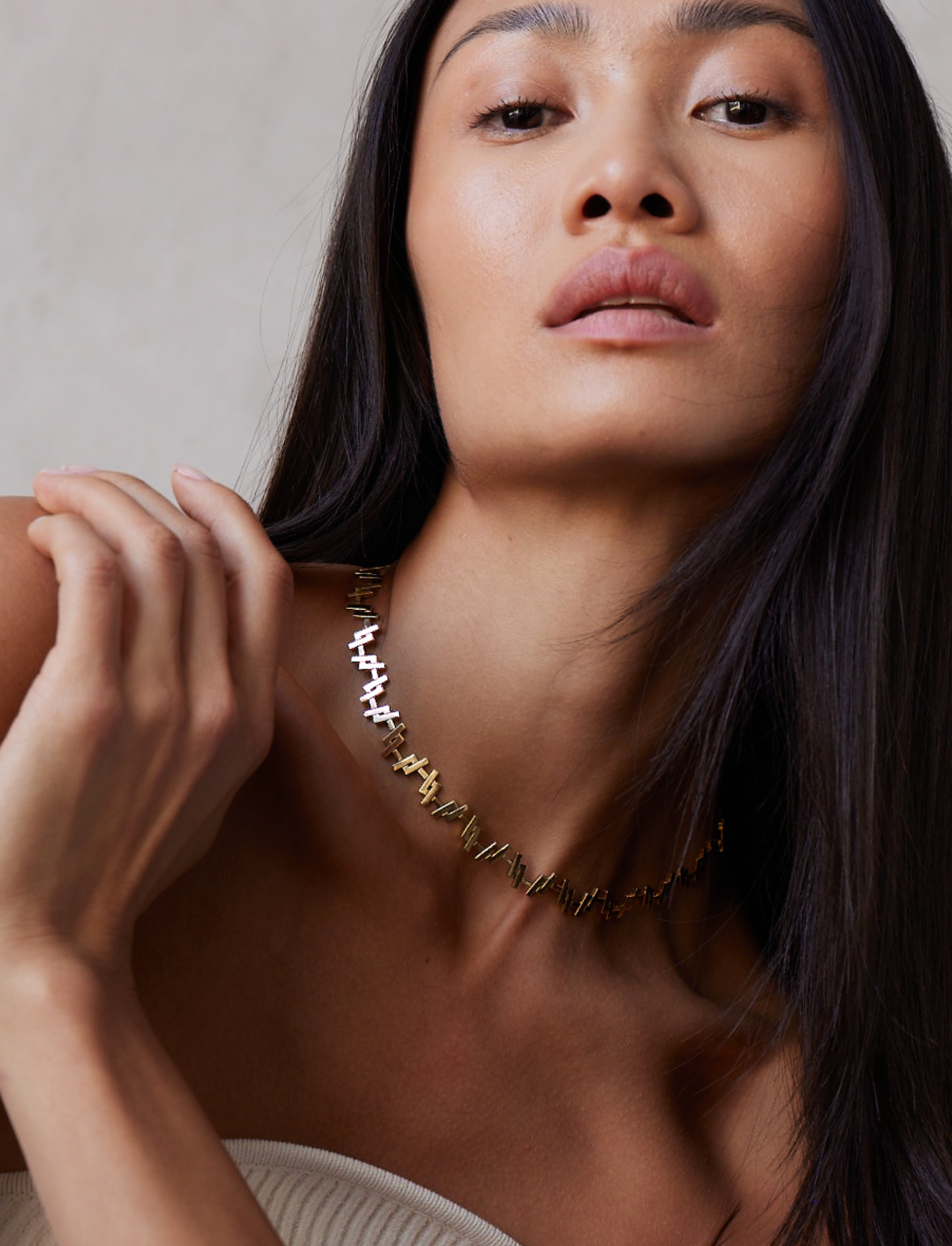 A woman wearing a solid yellow gold necklace with elongated matchstick-like links, designed in a Art Deco style.
