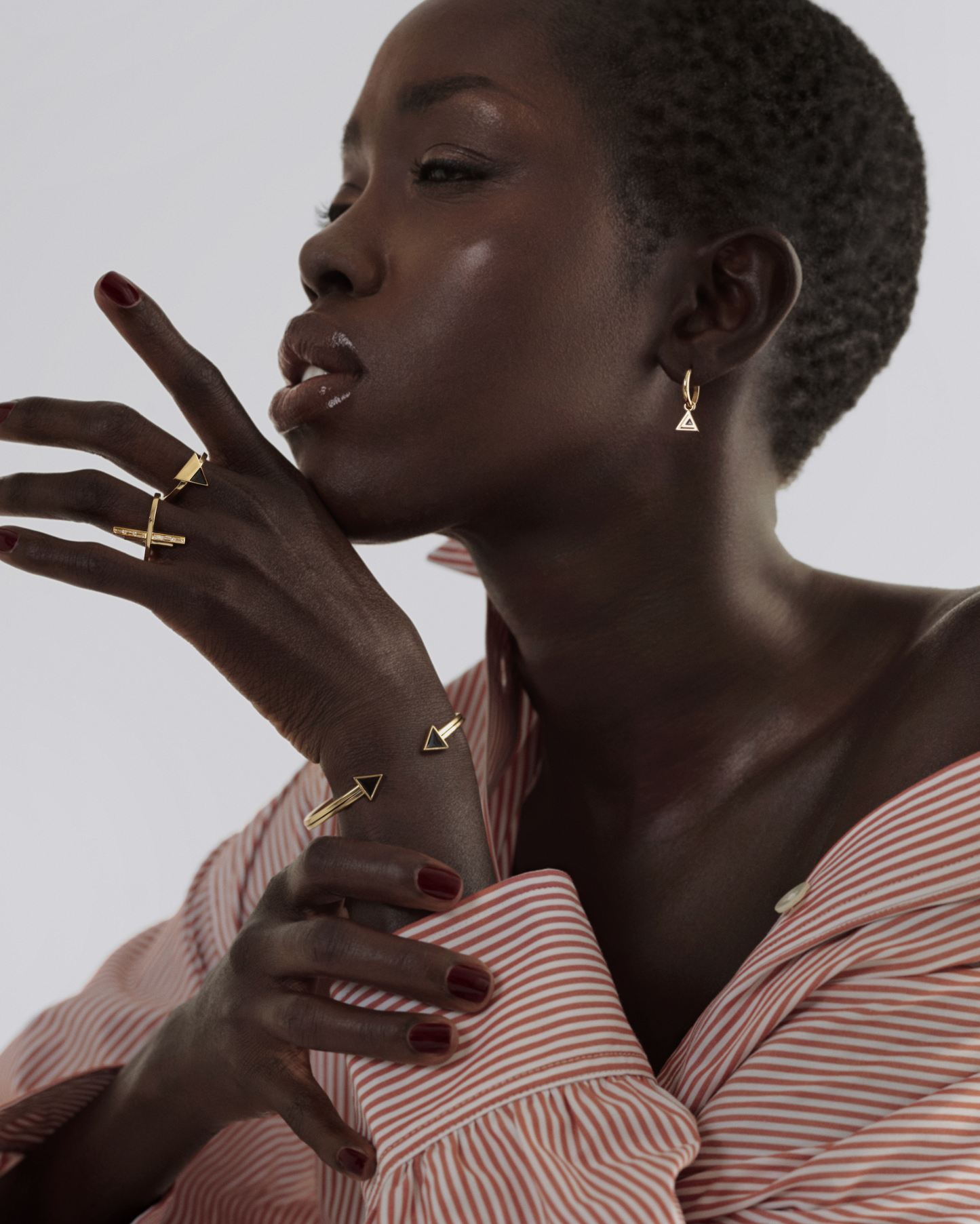 A model shot gold ring with a geometric design featuring two vertical polished gold bars and one horizontal bar set with baguette cut emeralds