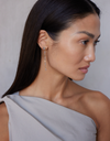 A model wearing a  pair of white gold earrings featuring kite-shaped white diamonds and white enamel details.