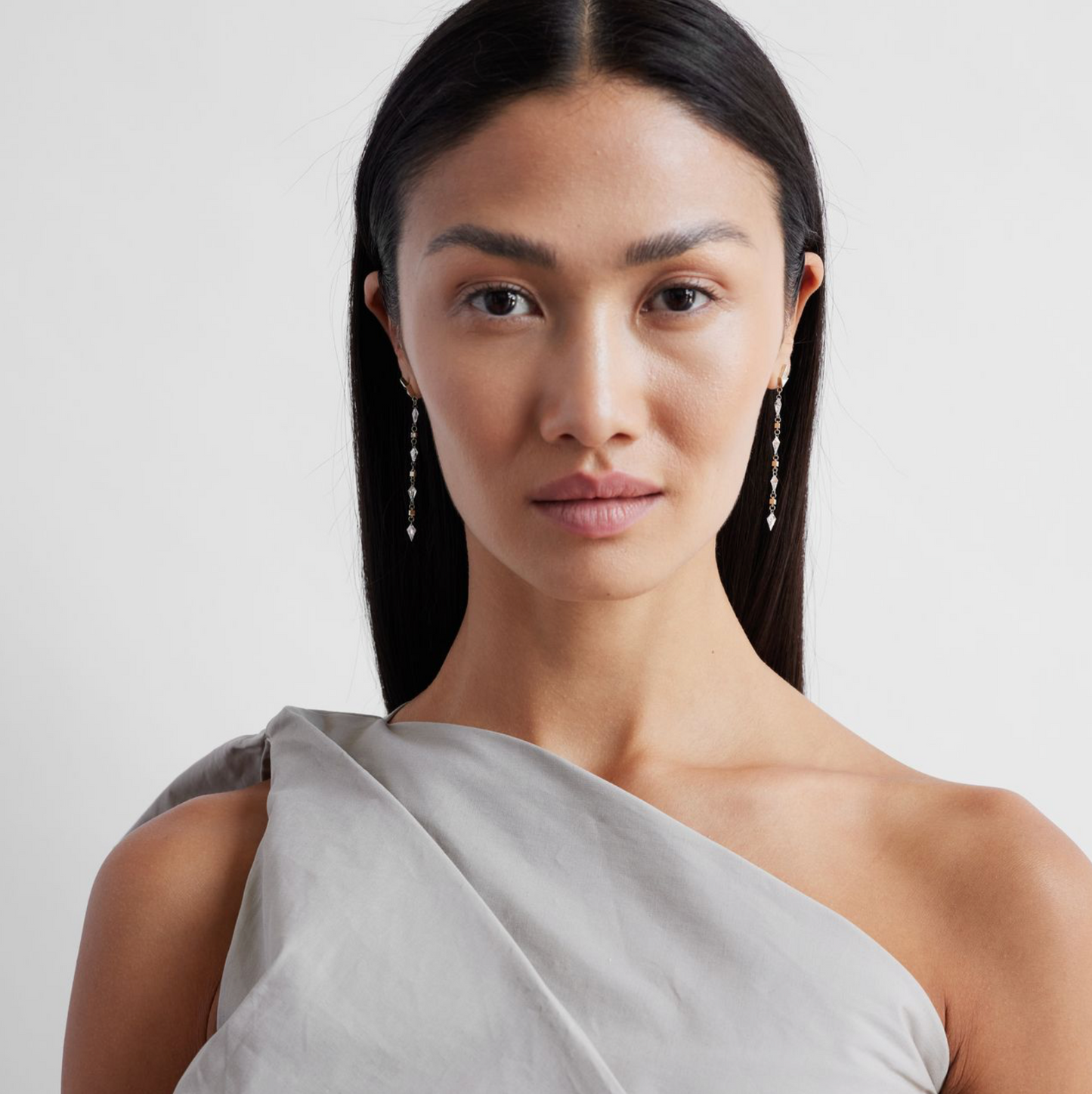 model wearing a pair of white gold earrings featuring kite-shaped white diamonds and white enamel details.
