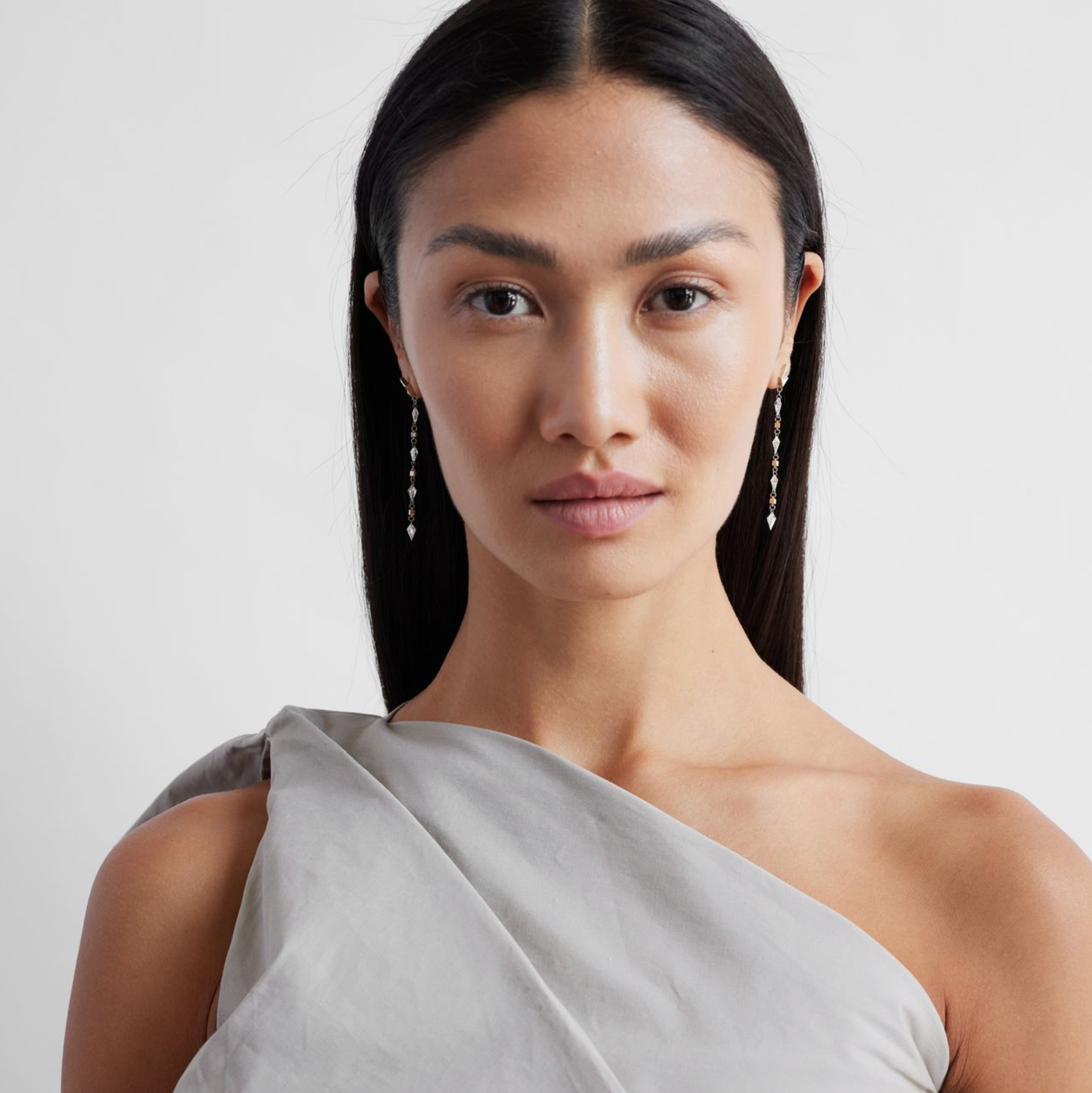 model wearing a pair of white gold earrings featuring kite-shaped white diamonds and white enamel details.