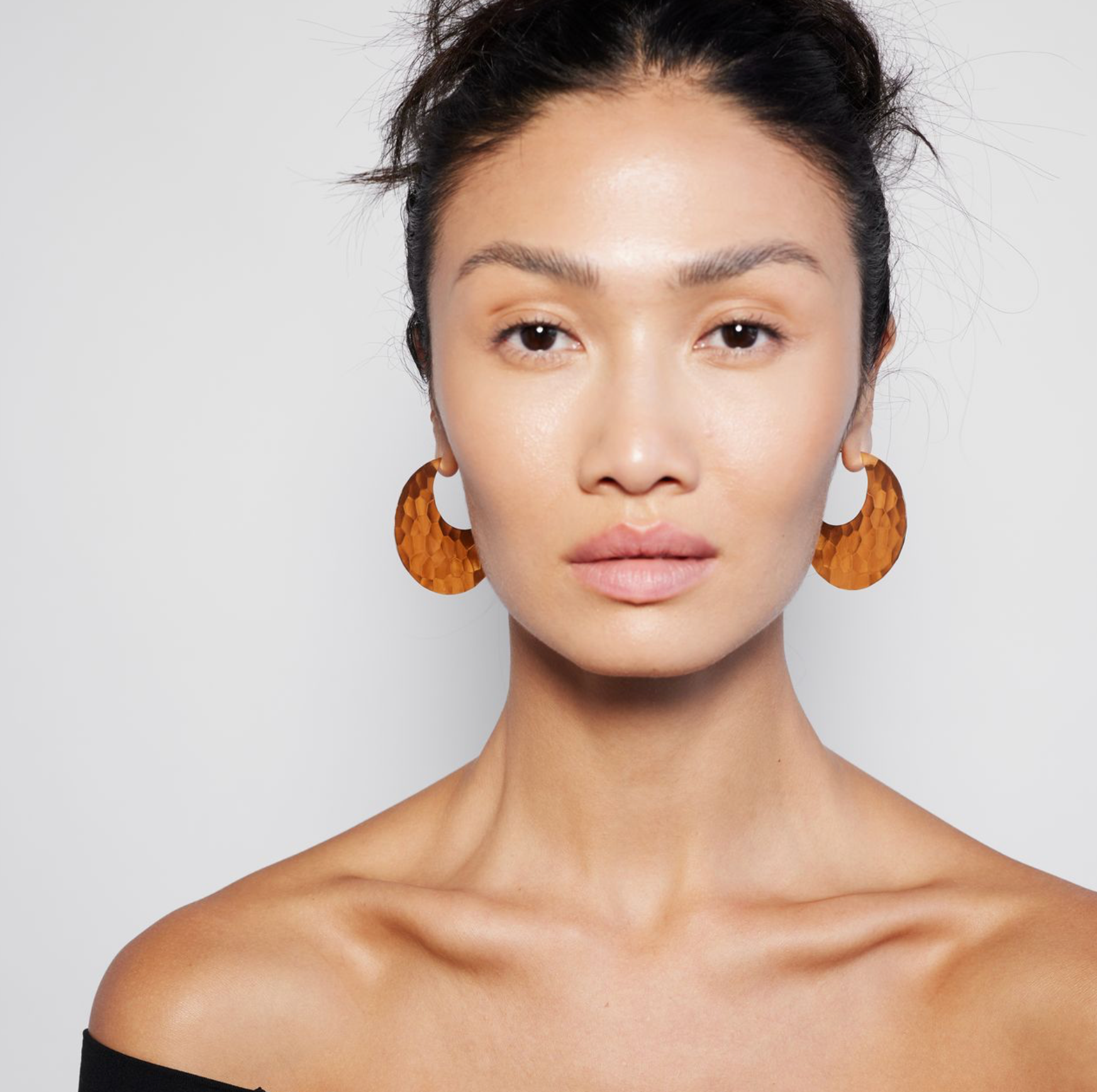 A person wearing a pair of gold hoop earrings.