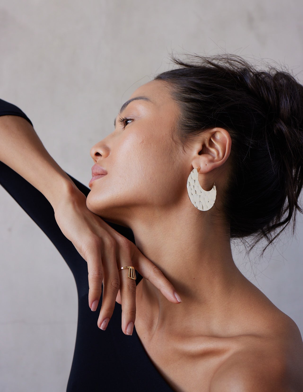 A model wearing a pair of 14K solid gold hammered hoop earrings with a textured surface, displayed against a white background.