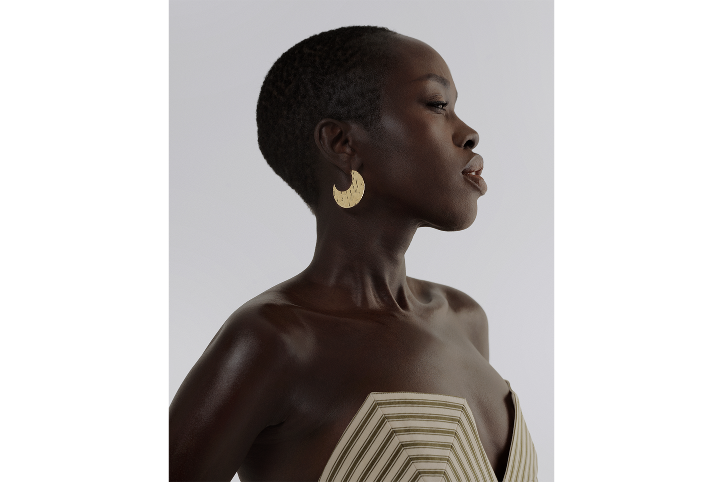 A model wearing a pair of 14K solid gold hammered hoop earrings with a textured surface, displayed against a white background.