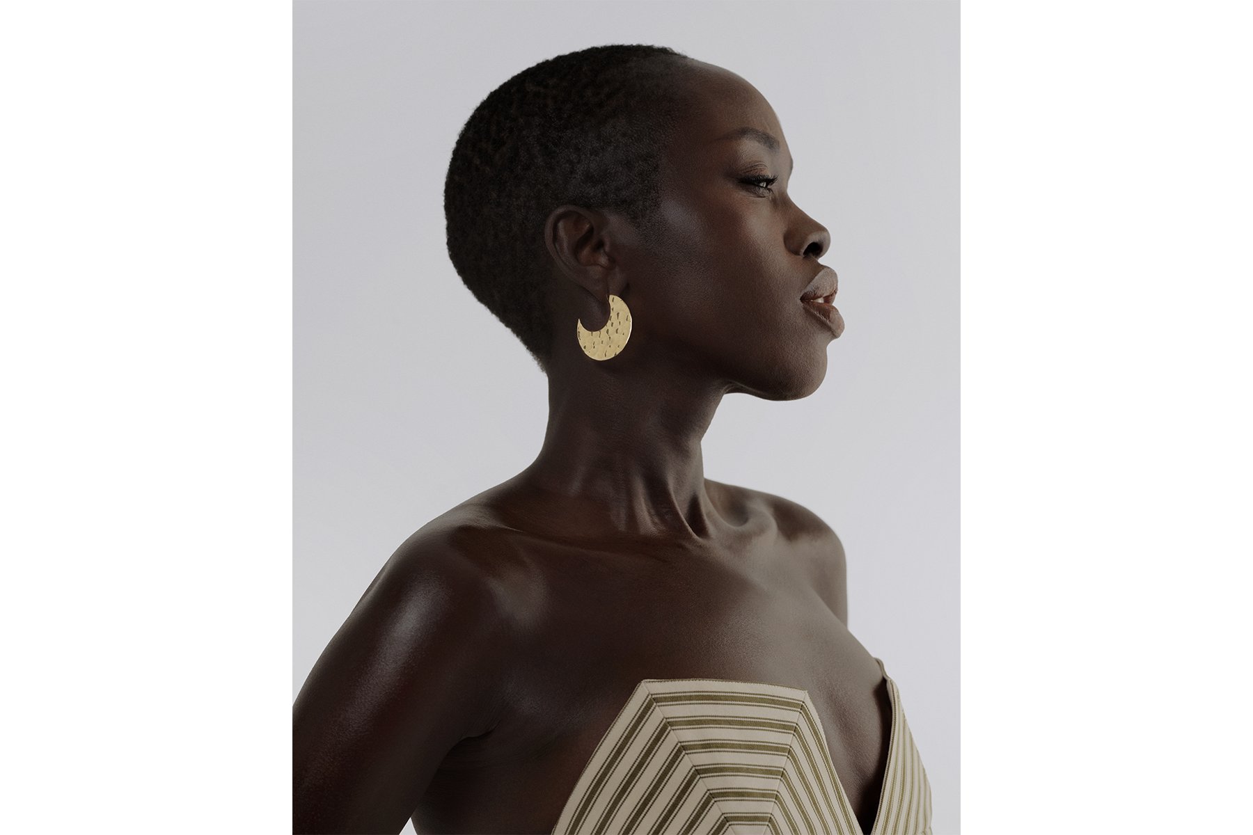 A model wearing a pair of 14K solid gold hammered hoop earrings with a textured surface, displayed against a white background.