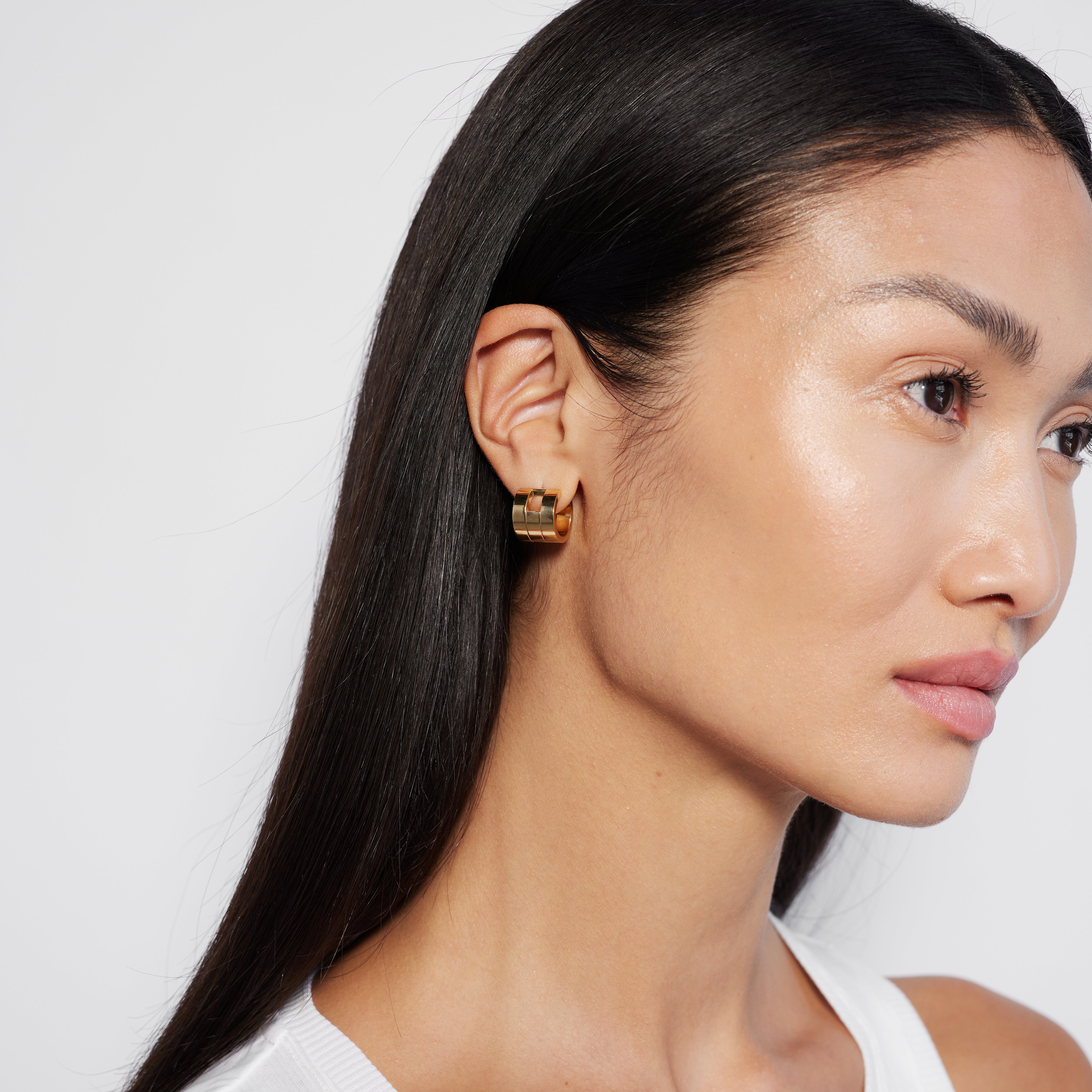A person wearing a single multi band gold hoop earring.