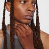 A close-up image of a person with their hand touching their chin, wearing a gold ring on their ring finger.