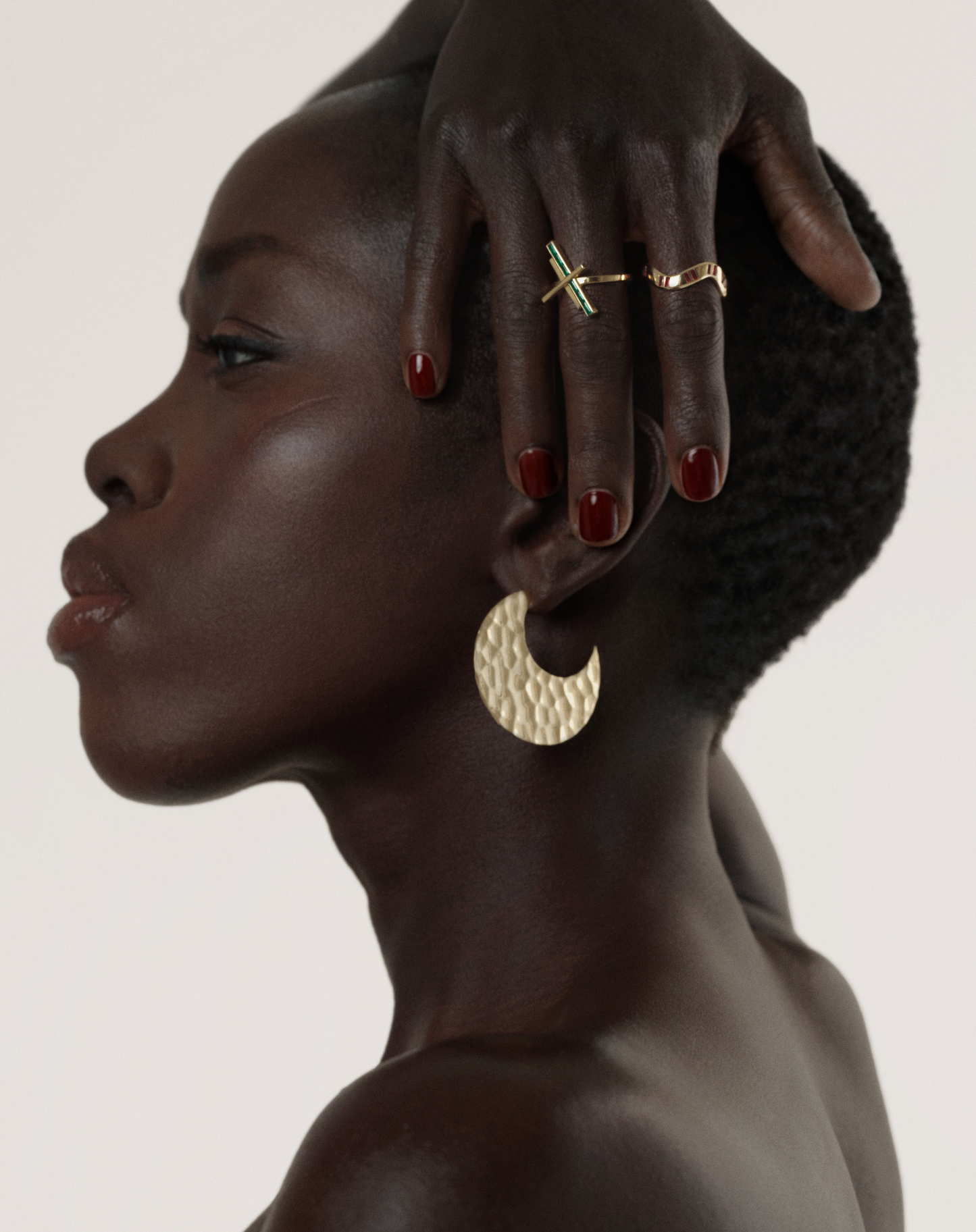 A person with a short haircut wearing a gold ring on their finger and a large gold hoop earring.