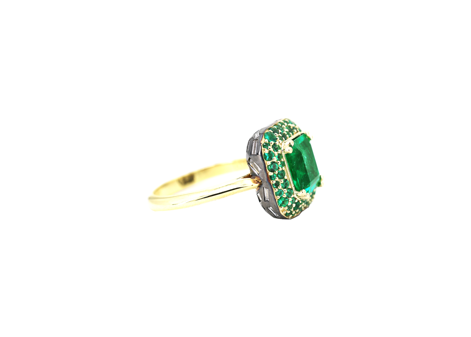 A ring featuring an octagon cut Zambian natural emerald, set on a domed halo with pave emeralds and a band of baguette natural diamonds, all in yellow gold.