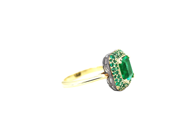 A ring featuring an octagon cut Zambian natural emerald, set on a domed halo with pave emeralds and a band of baguette natural diamonds, all in yellow gold.