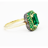 An elegant gold ring featuring an octagon cut Zambian natural 2ct emerald on a domed halo with pave emeralds and baguette natural diamonds set on the underside, with a 2mm band swooping up to ridged shoulders.