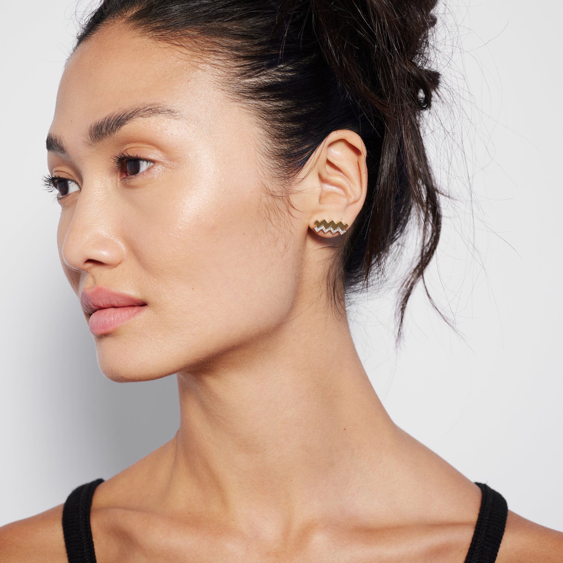A person wearing a single gold stud earring with a diamond pattern.