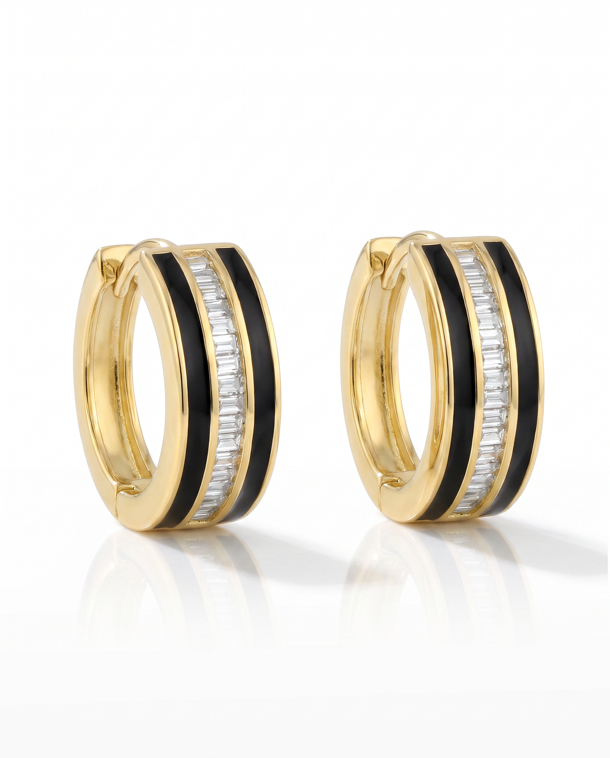 A pair of gold huggie hoop earrings with black enamel inlay and baguette-cut diamond stones, shown on a clean white background with a soft reflection.